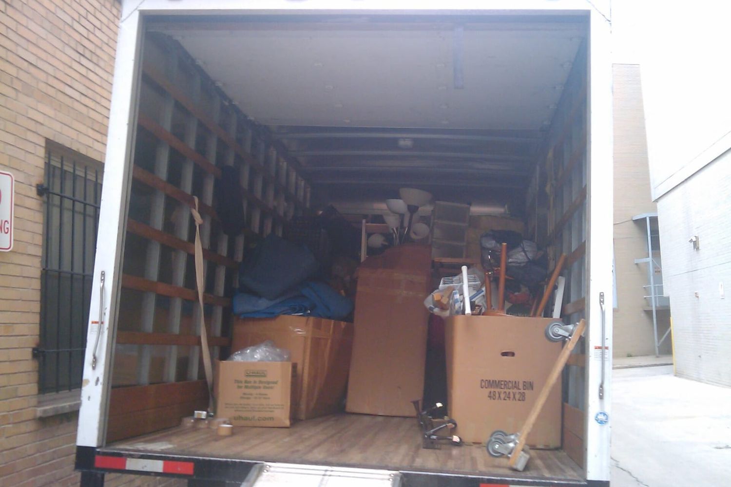 Open moving truck loaded with cardboard boxes, a lamp and furniture