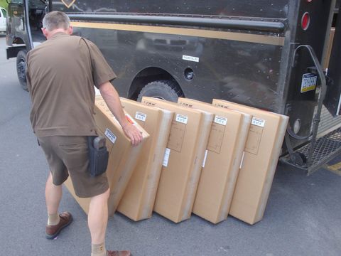 Delivery driver lining up six large labelled boxes beside a brown delivery truck