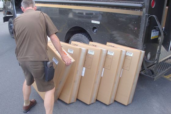 Delivery driver lining up six large labelled boxes beside a brown delivery truck