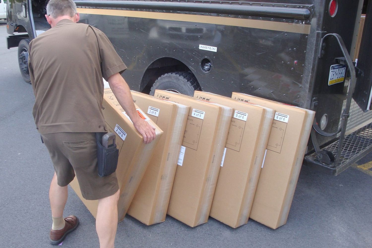 Delivery driver lining up six large labelled boxes beside a brown delivery truck