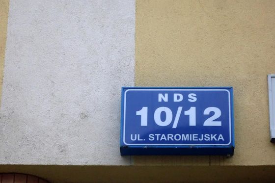 Blue house sign reading NDS 10/12 ul. Staromiejska on a yellow wall in Gdynia