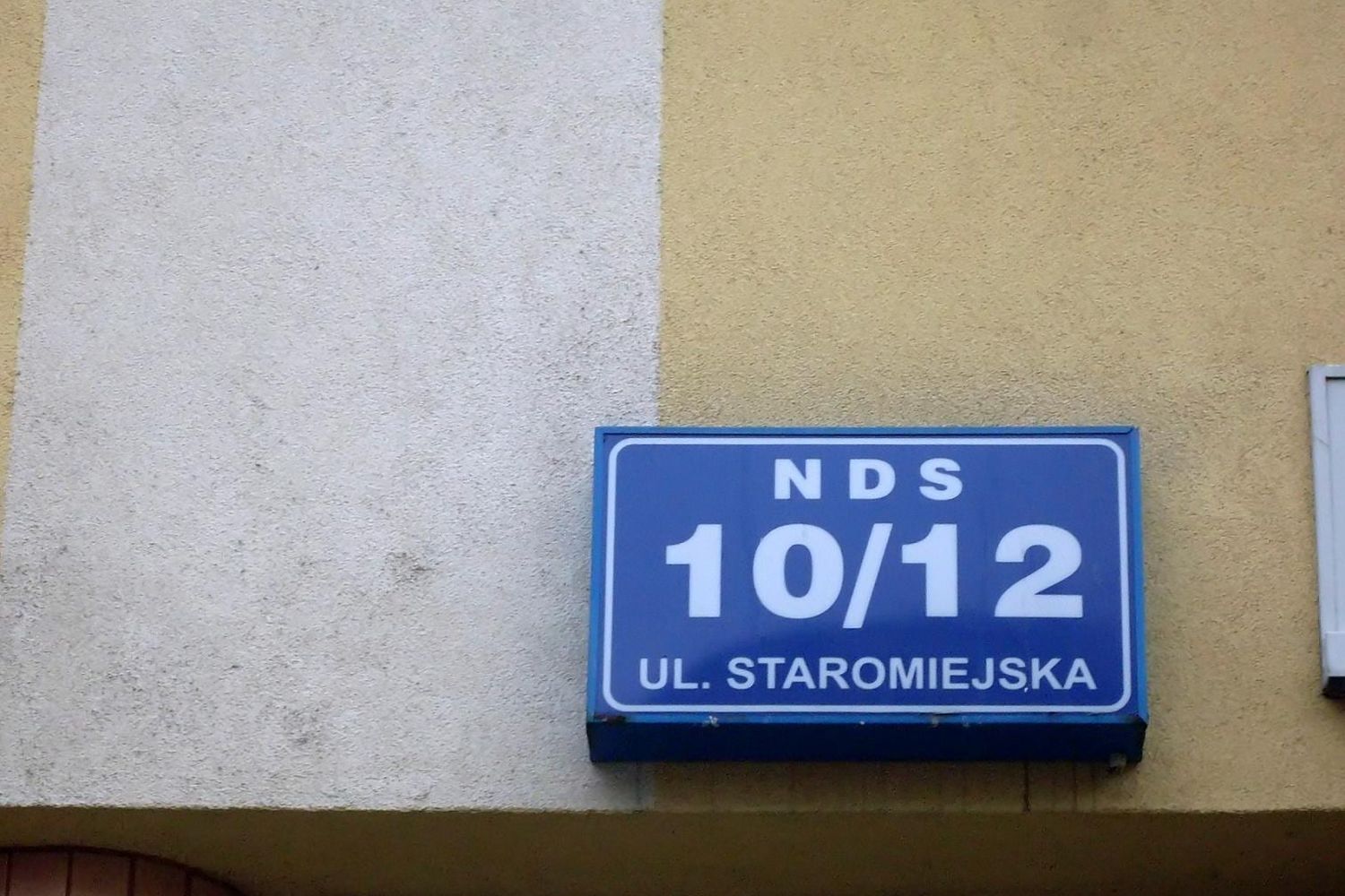 Blue house sign reading NDS 10/12 ul. Staromiejska on a yellow wall in Gdynia